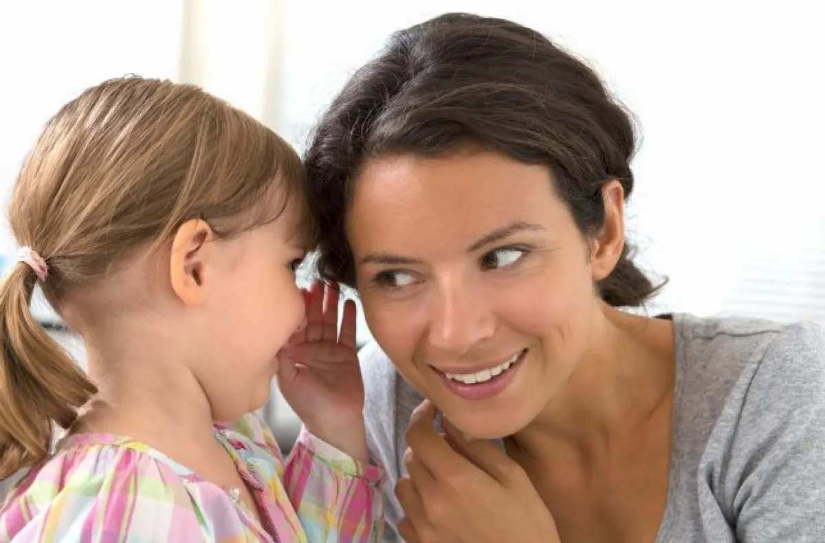 Dziewczynka opowiadająca coś na ucho mamie.