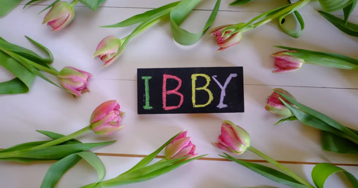 Kolorowy napis IBBY napisany kredą pomiędzy tulipanami leżącymi dookoła.