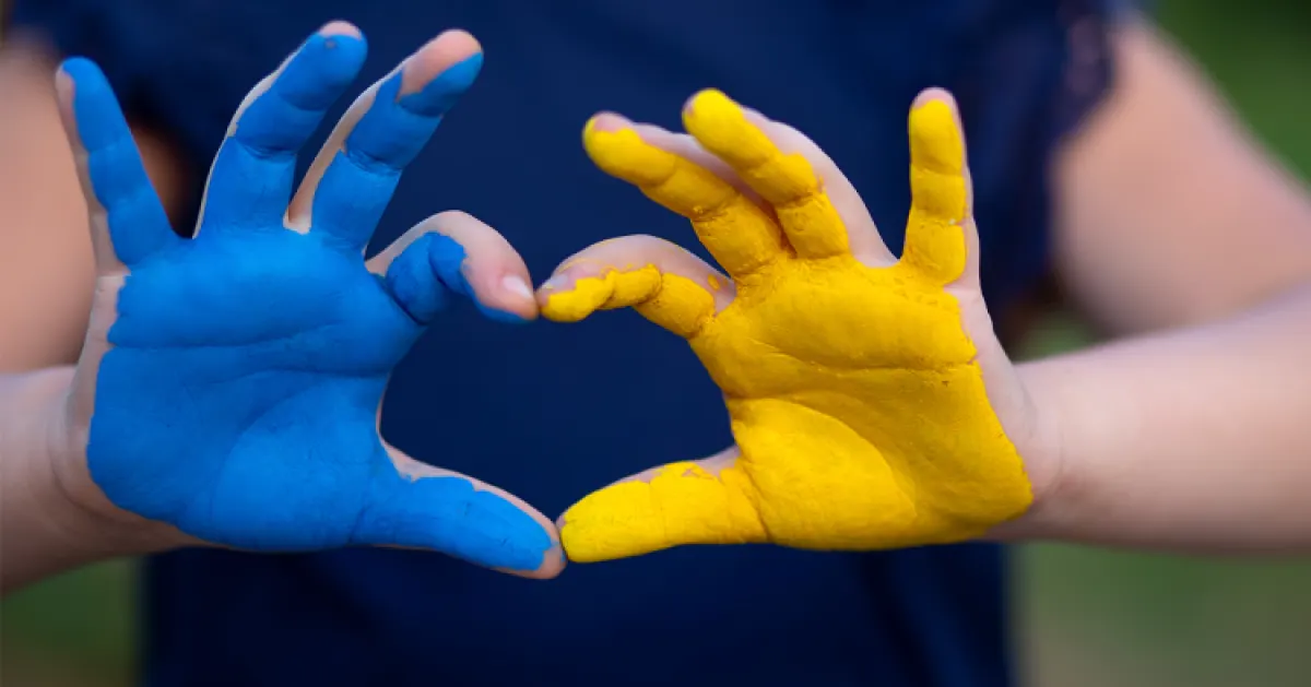 Dziecięce dłonie ułożone w kształt serca, pomalowane na niebiesko i żółto, w kolory flagi Ukrainy.