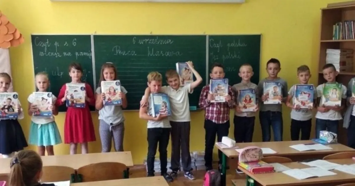 Rząd dzieci stojących w klasie lekcyjnej z podręcznikami Nowej Ery w rękach.