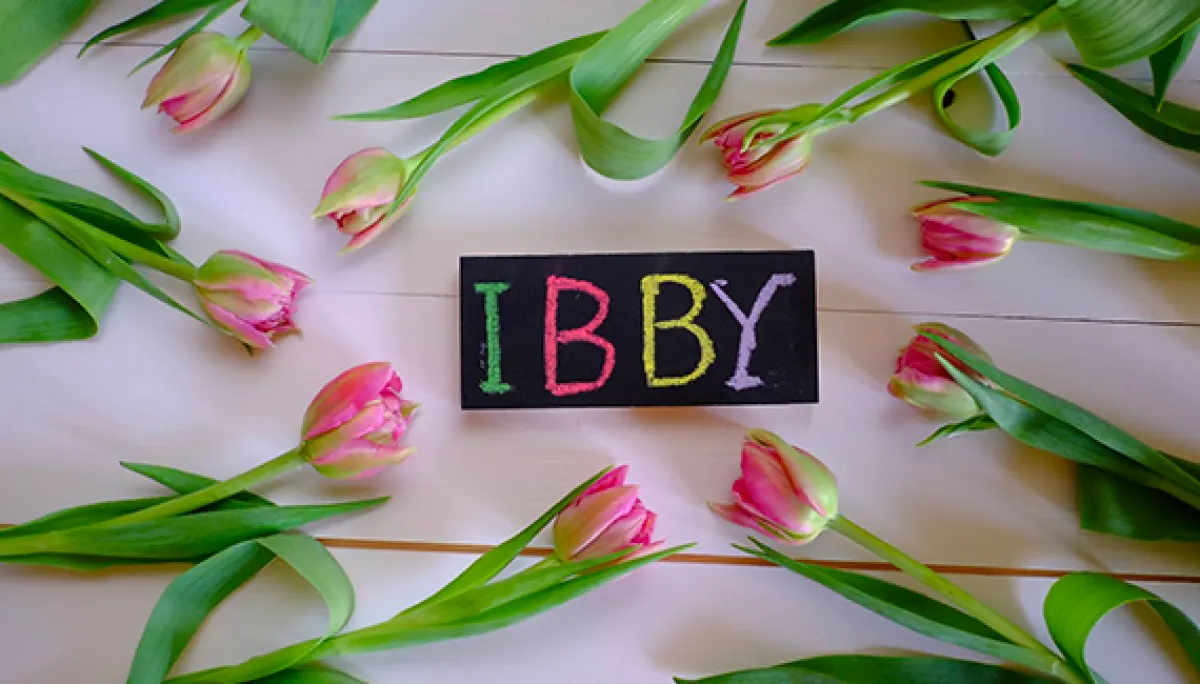 Kolorowy napis IBBY napisany kredą pomiędzy tulipanami leżącymi dookoła.